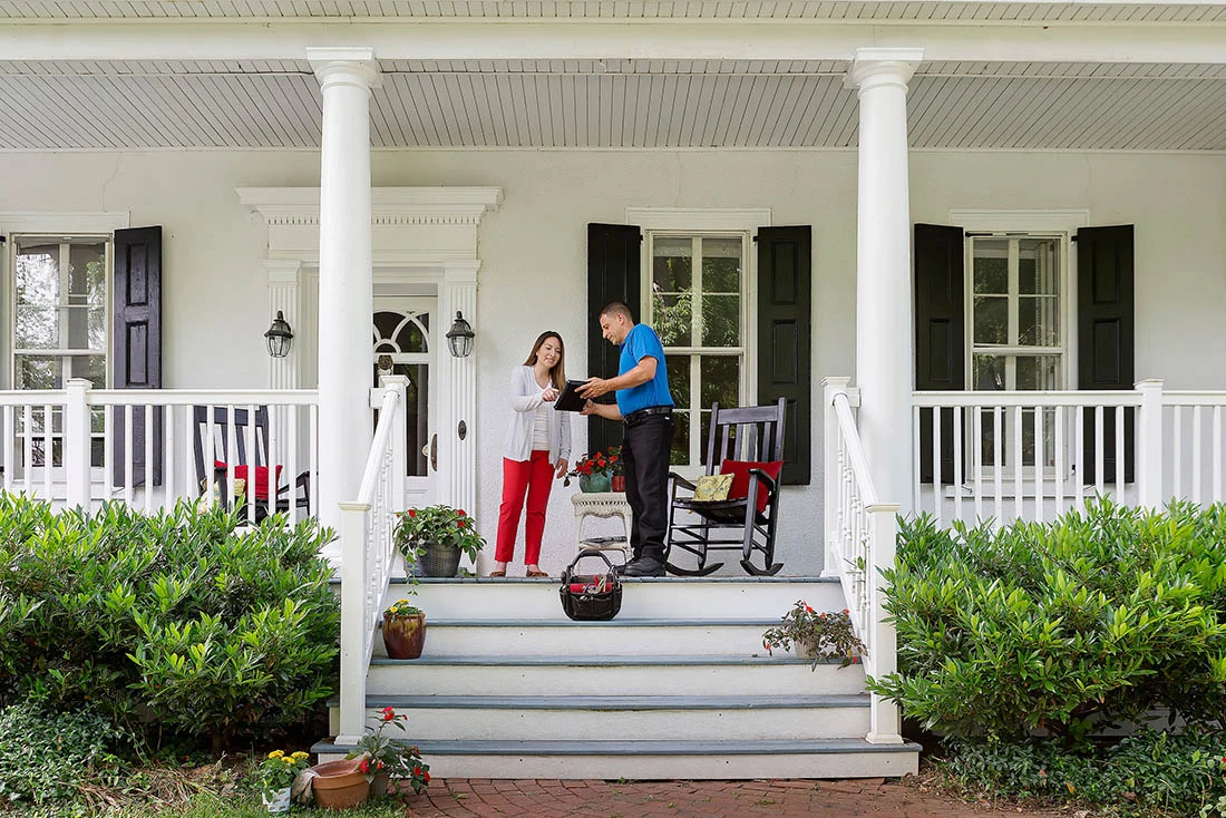 About Us Call Out Homeowner standing on front porch discussing HVAC service with a technician
