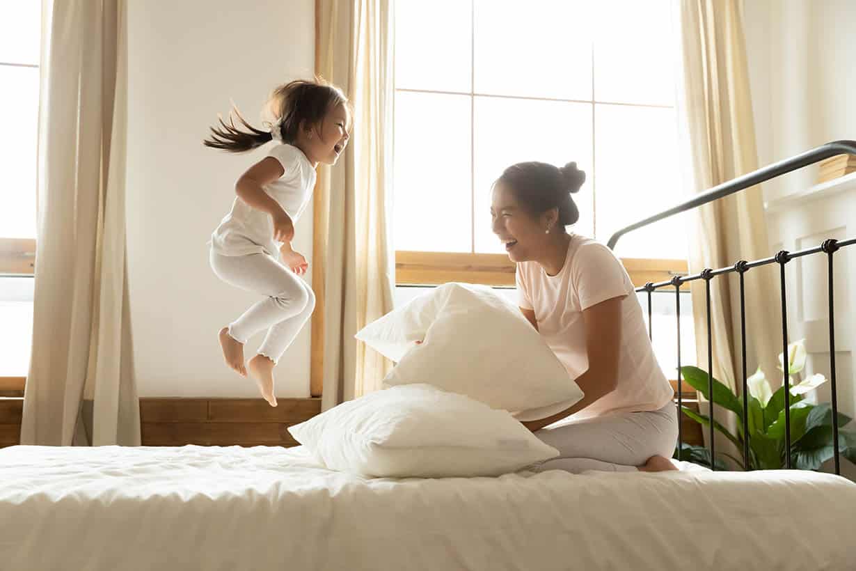 Carefree small daughter jump on bed while vietnamese mother laughing Carefree small daughter jump on bed while vietnamese mother laughing
