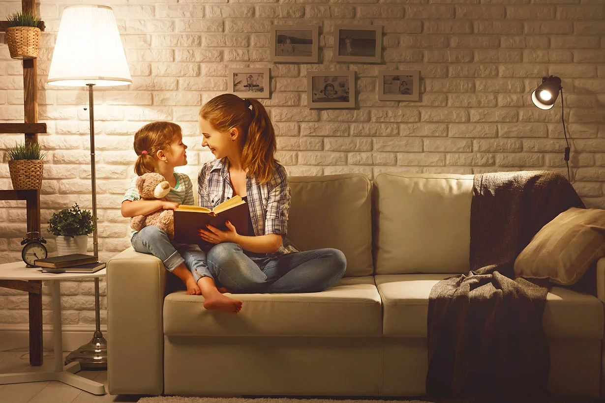 Family before going to bed mother reads to her child daughter book near a lamp in the evening mother reading to her daughter on the couch