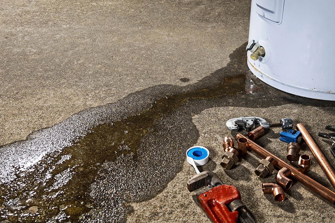 A leaking faucet on a domestic water heater with tools and fittings to replace appliance A leaking faucet on a domestic water heater with tools and fittings to replace water heater