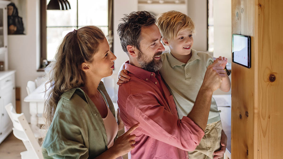Family looking at smart thermostat, adjusting or lowering heating temperatures at home.